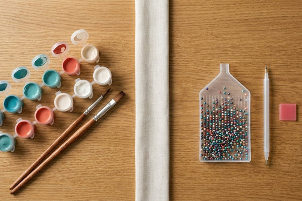 Overhead split comparison: acrylic paint pots and brushes on the left, a tray of coloured diamond painting drills with applicator pen and wax on the right