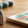 Close-up still life of a varnish spray can beside the glossy, freshly sealed corner of a paint by numbers canvas with abstract teal and coral paint blocks